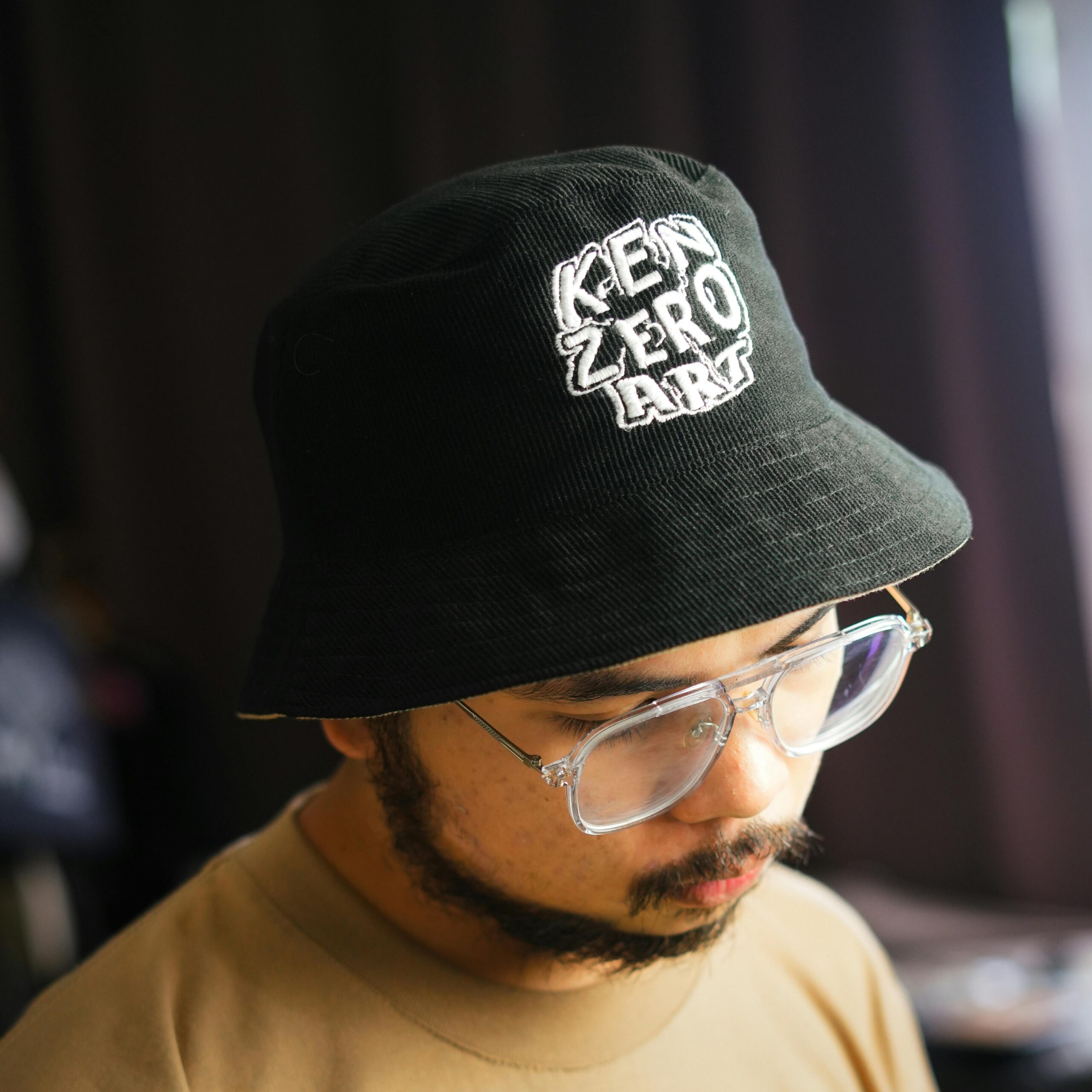 A portrait of an Asian man in a black bucket hat and glasses, blending casual style with fashion.